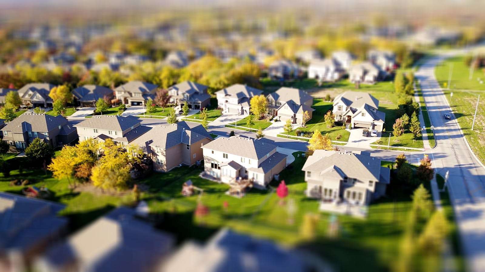 Aerial view of a suburban neighborhood with rows of similar houses, lush green lawns, and winding roads under a clear sky, subtly contrasting the struggles faced by some due to HUD housing rejection.