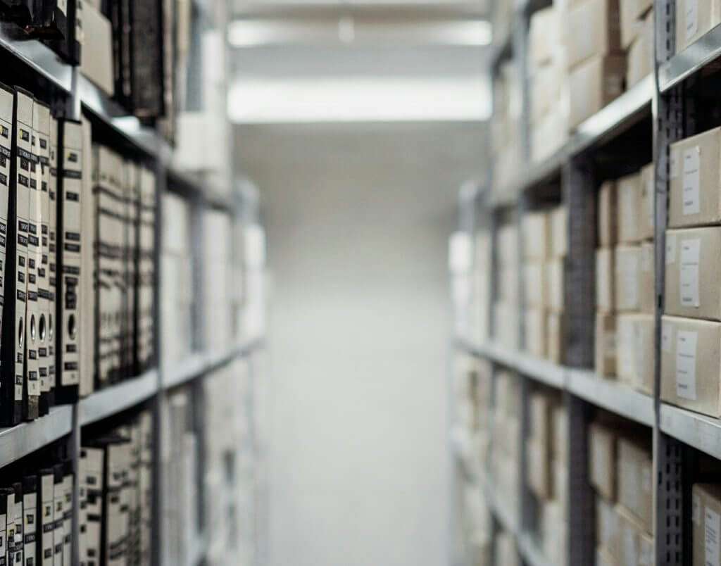 A narrow aisle with shelves on both sides, filled with organized folders and boxes detailing Section 8 facts, in a dimly lit storage room.