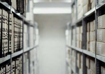 A narrow aisle with shelves on both sides, filled with organized folders and boxes detailing Section 8 facts, in a dimly lit storage room.
