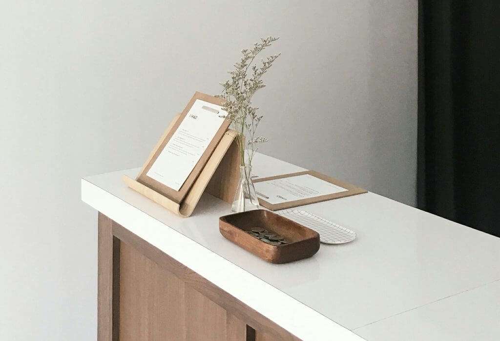 A minimalist desk features a wooden organizer, small plant, document holder, and tray with keys on a white surface, creating a calm workspace ideal for a Section 8 landlord managing HUD housing documents.