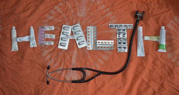 The word "HEALTH" is spelled out using various medication blister packs, tubes of ointment, and a stethoscope on an orange background, symbolizing the importance of well-being in affordable housing communities.