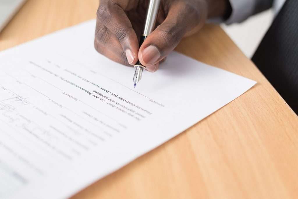 A person meticulously signs a Section 8 form with a pen on a wooden desk.