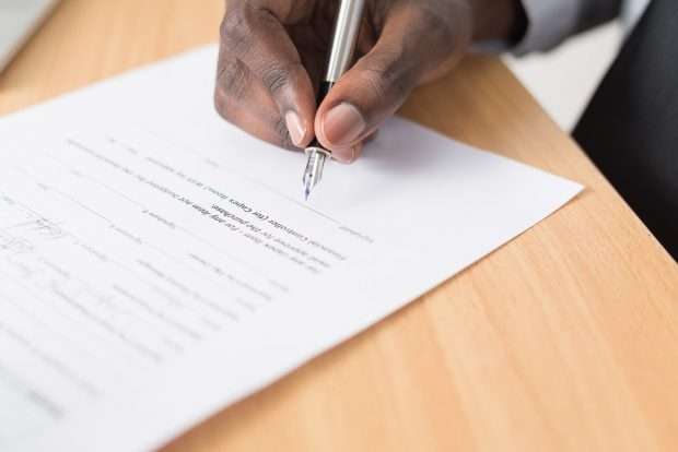 A person meticulously signs a Section 8 form with a pen on a wooden desk.