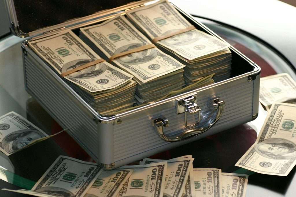 An open metal briefcase overflowing with stacks of 100-dollar bills rests on a glass table, resembling an unexpected windfall reminiscent of Section 8's hopes of earning money, with additional bills casually scattered around.