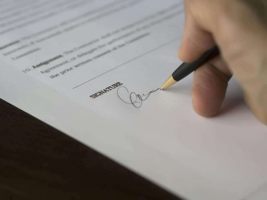A person is signing a document with a black pen on a wooden table, ensuring all Section 8 housing reporting requirements are meticulously completed.