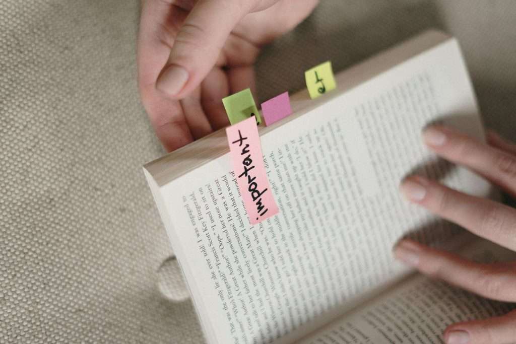Hands holding an open book, marked with pink, yellow, and green sticky notes, resemble the organization needed when navigating HUD housing resources.