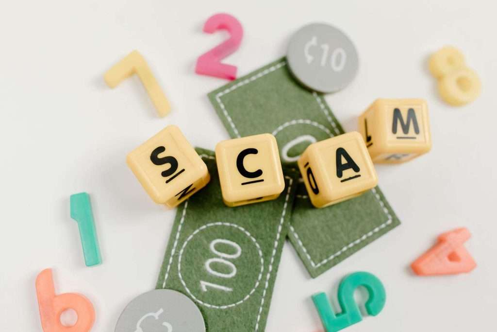 Scrabble tiles spelling "SCAM" sit on green play money, surrounded by colorful numbers, hinting at a HUD housing scam scene.