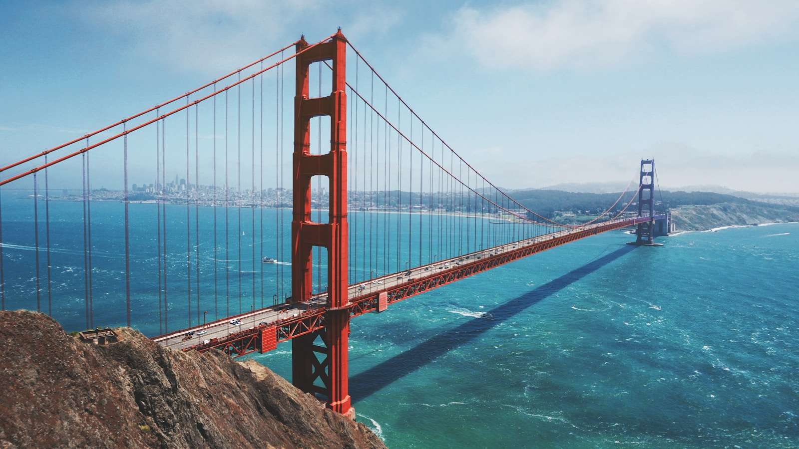 The Golden Gate Bridge spans a blue bay under a clear sky, connecting hilly landscapes, much like how Section 8 housing in California connects residents with diverse communities.
