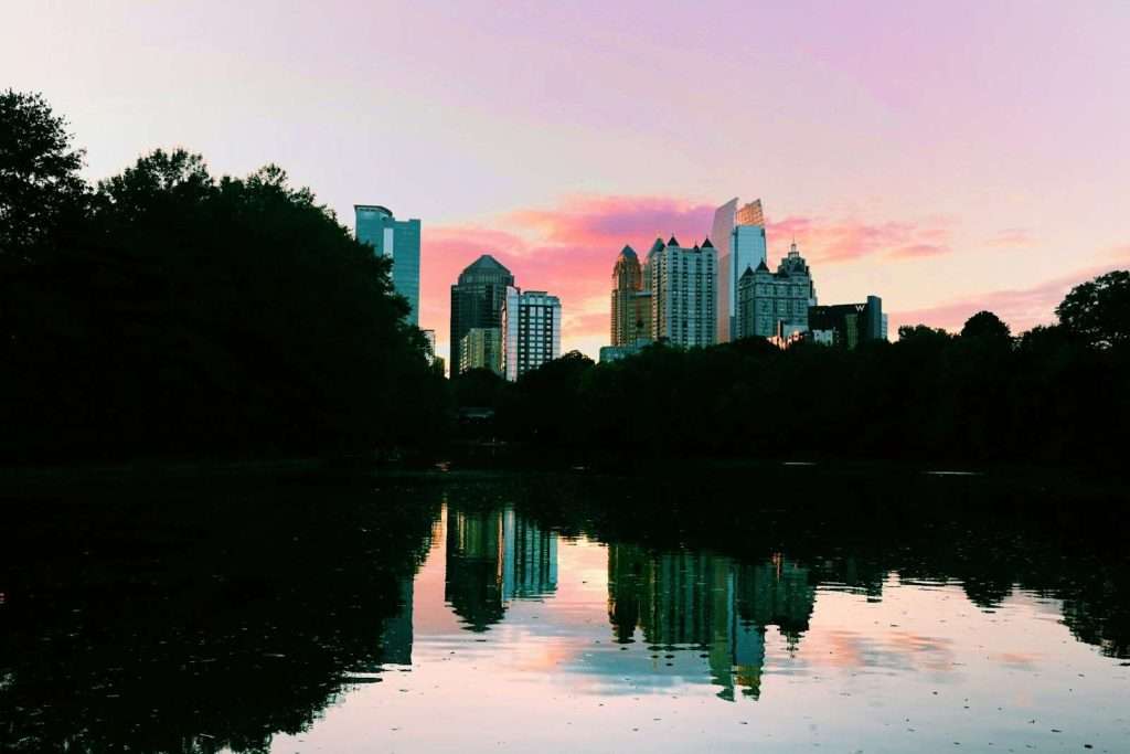 The city skyline at dusk, with a pink and purple sky reflected in a calm body of water, creates a serene backdrop for the silhouetted trees. Nearby, the community thrives with Section 8 housing in Georgia, seamlessly blending nature and urban living.