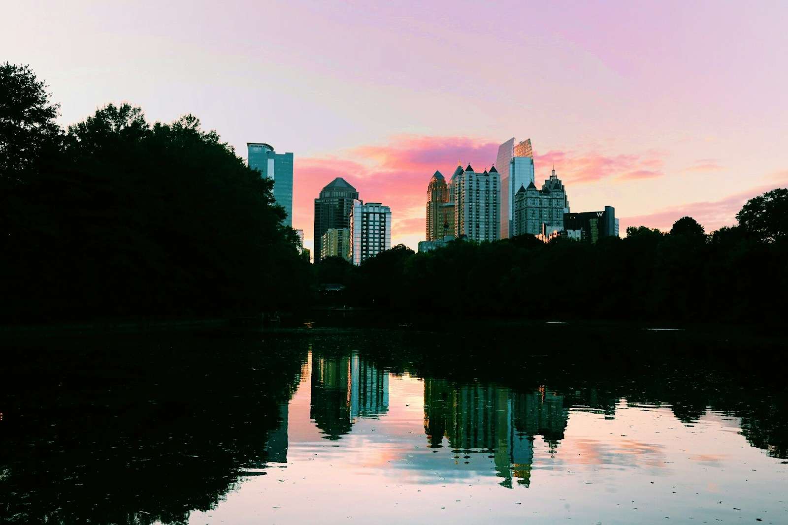 The city skyline at dusk, with a pink and purple sky reflected in a calm body of water, creates a serene backdrop for the silhouetted trees. Nearby, the community thrives with Section 8 housing in Georgia, seamlessly blending nature and urban living.