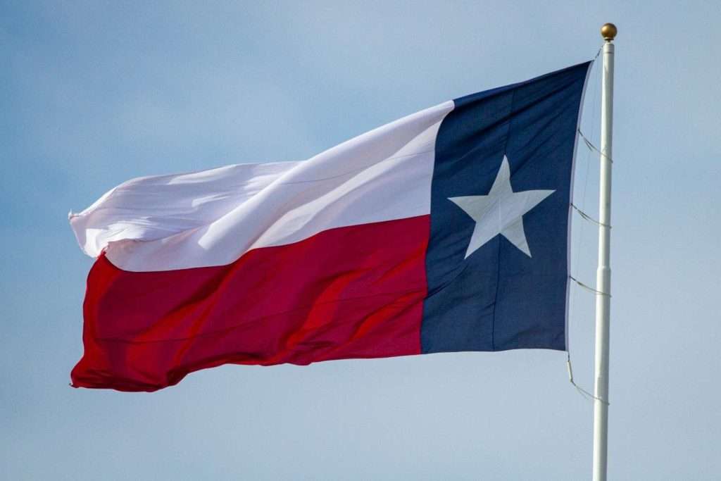 The Texas state flag, a proud emblem waving on a flagpole against a clear sky, symbolizes resilience much like the support provided by Section 8 in Texas.