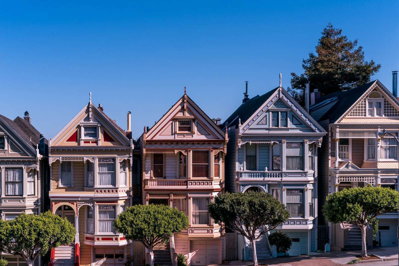 Row of colorful Victorian-style houses with gabled roofs under a clear blue sky, flanked by neatly trimmed trees, reminiscent of charming Section 8 California neighborhoods.